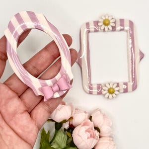 May include: Two decorative frames with a lavender and white striped pattern. One frame is oval-shaped with a solid lavender bow at the bottom. The other frame is rectangular with rounded corners and features a white daisy at the top and bottom.