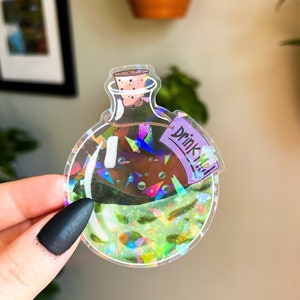 May include: A holographic sticker of a glass bottle with a cork stopper and a purple tag that says "Drink Me".