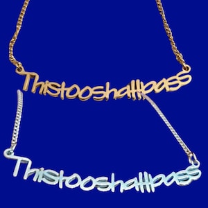 May include: Two necklaces with the phrase "This too shall pass" in a gold and silver finish. The gold necklace is on a gold chain, and the silver necklace is on a silver chain. The background is a solid blue.