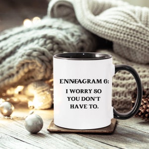 May include: White ceramic coffee mug with a black rim and handle. The mug has black text that reads "Enneagram 6: I worry so you don't have to."
