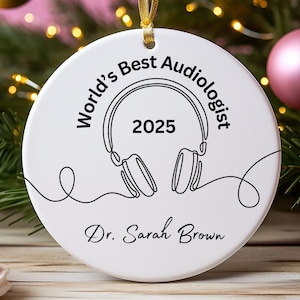 May include: White ceramic ornament with gold ribbon, featuring the text "World's Best Audiologist 2025" and a line drawing of headphones. The name "Dr. Sarah Brown" is printed below the headphones.
