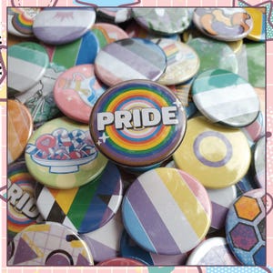 May include: A collection of colorful Pride-themed buttons. The central button displays the word "PRIDE" in white against a rainbow background. Other buttons feature various designs, including stripes, flags, and illustrations, in a variety of colors.