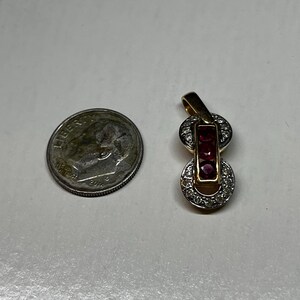 May include: A gold pendant with a red ruby and clear diamonds. The pendant is shaped like a figure eight.