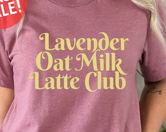 May include: A mauve t-shirt with the text "Lavender Oat Milk Latte Club" in a yellow font.