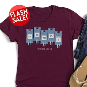 May include: A maroon t-shirt with a graphic of five IV bags labeled "LEVO", "NEO", "VASO", "EPL", and "JC". The text "#FIFTHPRESSOR" is printed below the graphic.