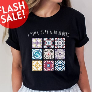 May include: Black t-shirt with the text "I still play with blocks" and a graphic of nine colorful patterned tiles.