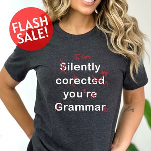 May include: A dark gray t-shirt with the text "I am silently corrected you're Grammar" printed on it. The text is crossed out in red.