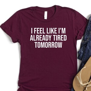 May include: A maroon t-shirt with white text that reads "I feel like I'm already tired tomorrow".