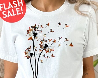 May include: A white t-shirt with a graphic of a dandelion made up of small, colorful birds. The dandelion is blowing in the wind and the birds are flying away.