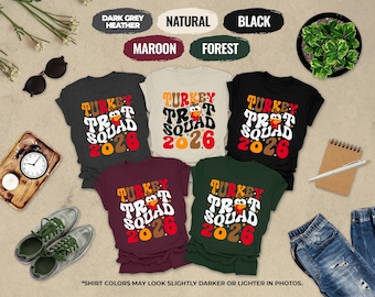 May include: Five t-shirts in dark grey heather, natural, black, maroon, and forest green. Each shirt features a graphic with the text "TURKEY TROT SQUAD 2026" in a wavy font, accompanied by a cartoon turkey illustration with red and yellow accents.