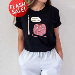 a woman wearing a black t - shirt with a knitting needle and ball of yarn