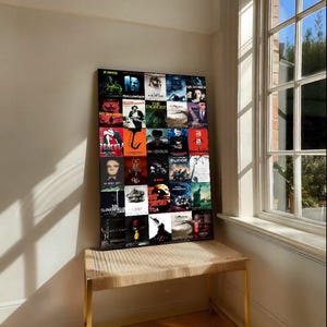 May include: A framed collage of horror movie posters, including "Halloween" and "The Exorcist", displayed on a woven bench with gold legs. The artwork is against a neutral wall, near a window with natural light.