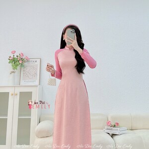 Op de afbeelding: Een roze traditionele Vietnamese jurk, bekend als een Ao Dai, met lange mouwen en een hoge kraag. De jurk is gemaakt van een zijdeachtige stof en heeft een getailleerd bovenstuk en een zwierige rok. De jurk wordt gecombineerd met een bijpassende roze broek.