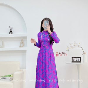 May include: A long, purple and pink floral print dress with a mandarin collar and long sleeves. The dress is called "Ao Dai by Emily".
