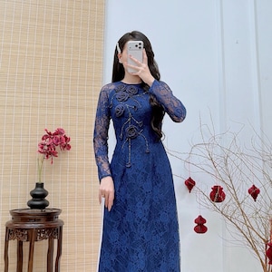 May include: A long, navy blue lace dress with long sleeves and a floral design. The dress features dark floral embellishments on the bodice. The website address AodaiEmily.com is visible on the dress.