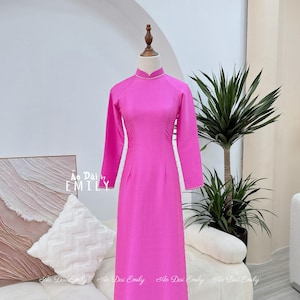 May include: A pink long-sleeved dress with a mandarin collar and pearl trim. The dress is on a mannequin and is displayed against a white background.