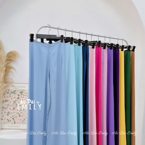 May include: A rack of ten pairs of wide-legged pants in various colors, including light blue, navy blue, pink, hot pink, lavender, purple, yellow, green, and brown. The pants are hanging on hangers and are all the same style.