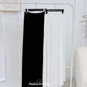 May include: Two pairs of wide-leg pants hanging on a white rack. One pair is black and the other is white.