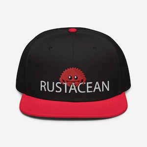 Puede incluir: Gorra de béisbol negra y roja con un cangrejo bordado en blanco y el texto "RUSTACEAN".