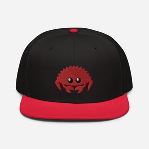 May include: A black and red baseball cap with a red embroidered crab on the front.