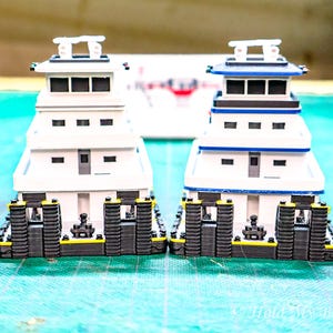 Può includere: Due modelli di rimorchiatori bianchi con dettagli neri e gialli. I rimorchiatori hanno più ponti e si fronteggiano.