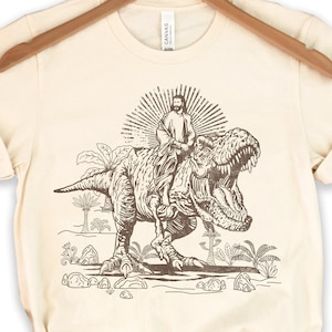 Jesus Riding T rex Dinosaur Shirt | Cool Tee Gift | Christ T-shirt | Funny Meme Shirts | Tyrannosaurus Rex Tshirt | Cute T-rex Animal Shirts