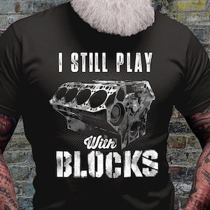 May include: A black t-shirt with a white graphic of an engine block and the text "I still play with blocks".