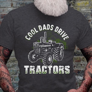 May include: A dark gray t-shirt with a distressed green graphic of a tractor and the text "Cool Dads Drive Tractors".