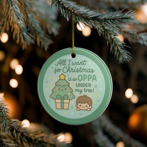May include: A round, green Christmas ornament with the text "All I want for Christmas is an OPPA under my tree!" features a cartoon Christmas tree and a small character. The ornament hangs from a gold string.