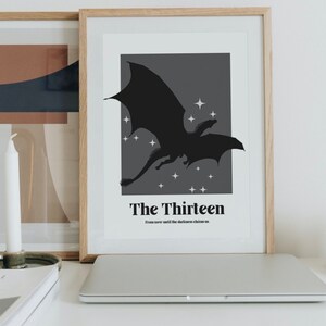 May include: A framed print featuring a black silhouette of a dragon flying against a dark grey background with white stars. The text "The Thirteen" and "From now until the darkness claims us." is printed below the dragon.