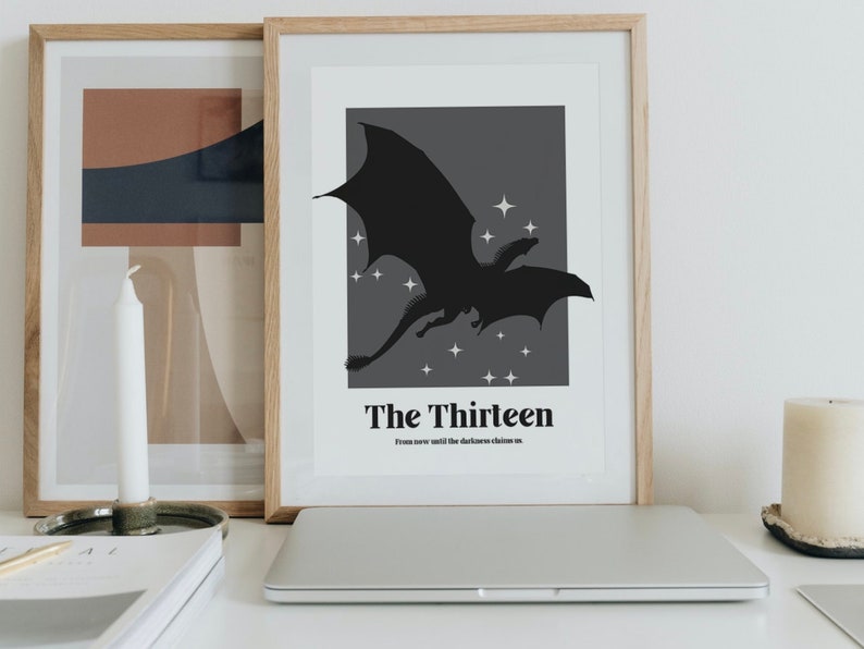 May include: A framed print featuring a black silhouette of a dragon flying against a dark grey background with white stars. The text "The Thirteen" and "From now until the darkness claims us." is printed below the dragon.