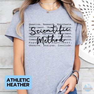 May include: Athletic heather gray t-shirt with the words "Scientific Method" in a cursive font. The shirt also has a list of scientific method steps in a black font. The words "Athletic Heather" are in a blue rectangle.