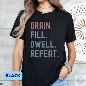 May include: Black t-shirt with the text "DRAIN. FILL. DWELL. REPEAT." in a vintage style font.