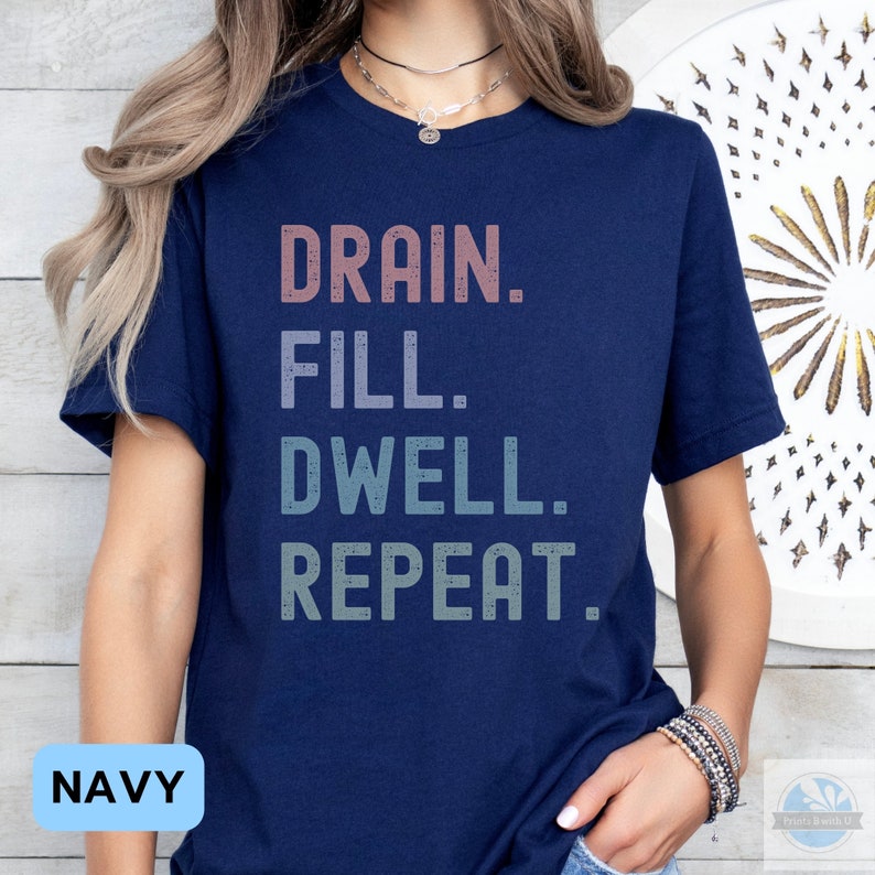 May include: A navy blue t-shirt with the text "DRAIN. FILL. DWELL. REPEAT." in a gradient of pink, blue, and green.