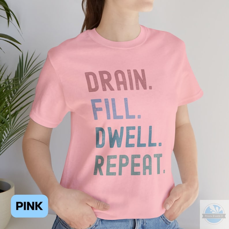 May include: Pink t-shirt with the text "DRAIN. FILL. DWELL. REPEAT." in a faded, layered font.