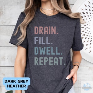May include: Dark grey heather t-shirt with the text "DRAIN. FILL. DWELL. REPEAT." in a vintage style font with a gradient of colors.