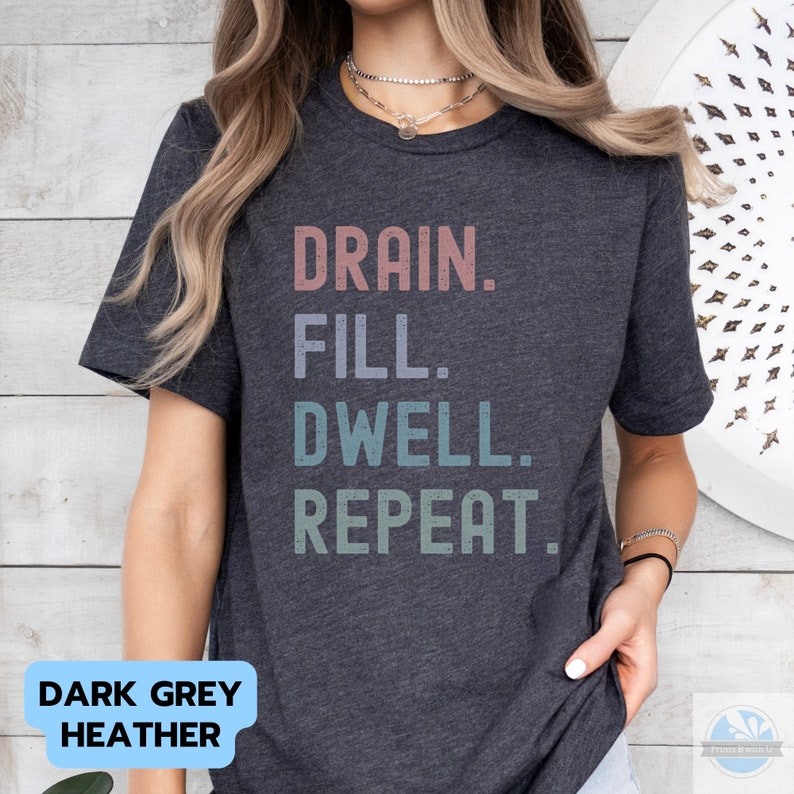 May include: Dark grey heather t-shirt with the text "DRAIN. FILL. DWELL. REPEAT." in a vintage style font with a gradient of colors.