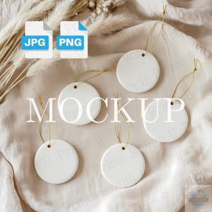 May include: A mockup featuring five white, round ceramic ornaments with gold string hangers. The word "MOCKUP" is displayed in large, white text. Two file type icons, JPG and PNG, are in the upper left corner. The ornaments rest on a cream-colored fabric.