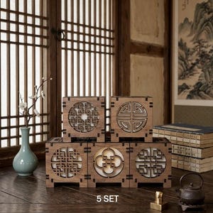 May include: A set of five square wooden lamps featuring intricate laser-cut geometric patterns on the front panels. Each lamp emits a soft white light through the cutouts. The set is arranged in a tiered formation with the text 5 SET below.