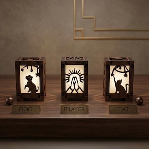 May include: Three rectangular wooden lanterns with internal illumination. The left lantern features a dog silhouette, the center shows hands in prayer under a sun, and the right displays a cat reaching for stars. Each has a label reading DOG, PRAYER, CAT.