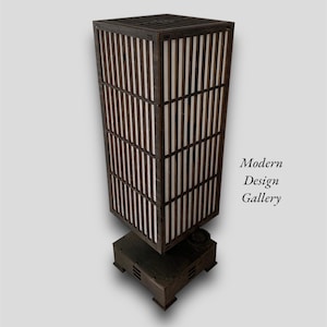 May include: A dark brown wooden floor lamp with a white paper shade. The lamp has a square base and a tall, rectangular shade with a grid pattern. The lamp is lit and casts a warm glow.