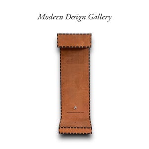 May include: A brown leather phone stand with a black stitched border and the text "Modern Design Gallery" on the front.