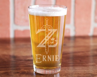 May include: A clear glass pint glass with a white design of a sword and the letter Z. The name "ERNIE" is etched below the design.