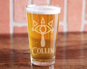 May include: A clear glass pint glass with a white etched design of a stylized eye with three triangles above it and the name "COLLIN" below. The glass is filled with a light yellow beer.