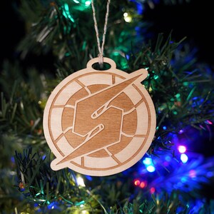 May include: A wooden Christmas ornament featuring a brown lightning bolt design in a circle. The ornament is hanging on a green Christmas tree with blue and red lights.
