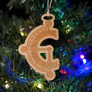 May include: A wooden Christmas ornament shaped like a stylized letter "G" with Roman numerals and other markings. The ornament is hanging on a green artificial Christmas tree.