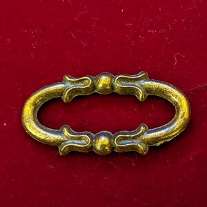 May include: A gold-toned metal oval-shaped pull with ornate detailing. The pull has two decorative knobs on either side.