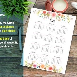 May include: A printable calendar for the year 2026 with floral illustrations. Each month is displayed in a separate box with a white background and black text. The calendar is decorated with watercolor flowers in shades of pink, orange, and blue.