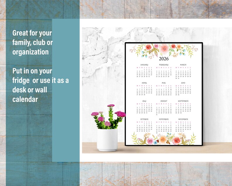 May include: Printable 2026 calendar with floral design. The calendar is framed and sitting on a white shelf. The calendar has a floral design at the top and bottom. The months are listed in a grid format.