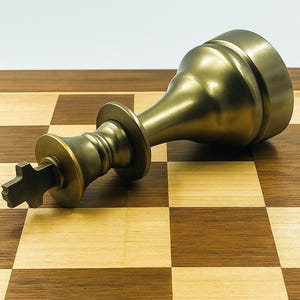 Peut inclure: Un roi d'échecs de couleur bronze couché sur un échiquier en bois. Le plateau comporte des cases marron clair et foncé alternées. La pièce du roi a une couronne détaillée et un sommet en forme de croix.